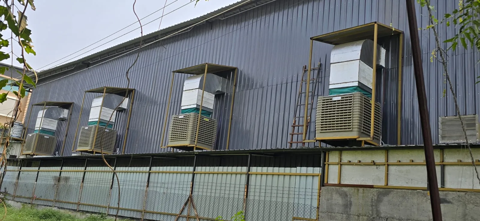 Industrial air coolers on steel frames with GI duct risers along a factory wall
