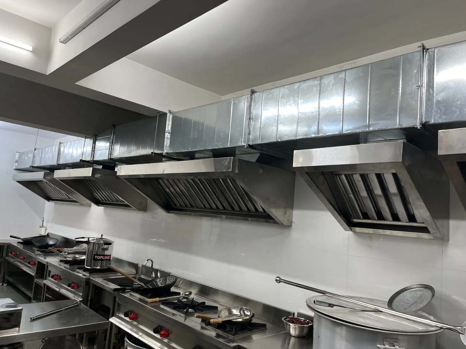 Stainless-steel commercial kitchen exhaust hoods with GI ducting above cooking range
